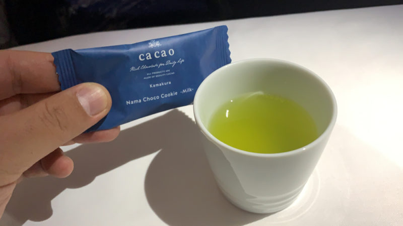 a hand holding a small blue packet next to a white cup of liquid