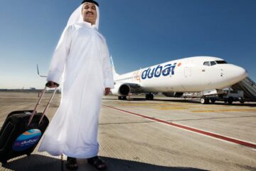 a man in a white robe with a suitcase standing in front of an airplane