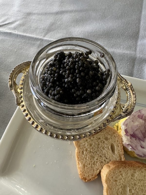 a glass jar with black caviar on a white plate