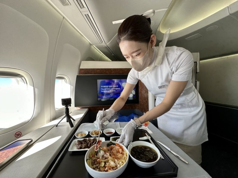 a woman wearing a mask and gloves preparing food in a plane