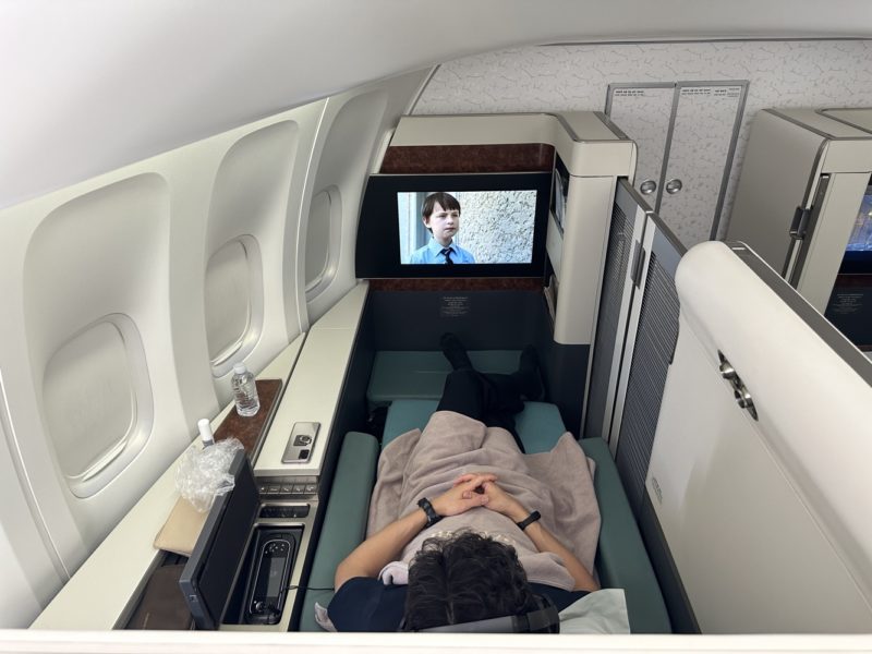 a person lying in a bed with a television on the side of the plane