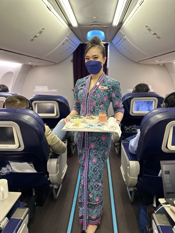 a woman wearing a face mask holding a tray of food in an airplane