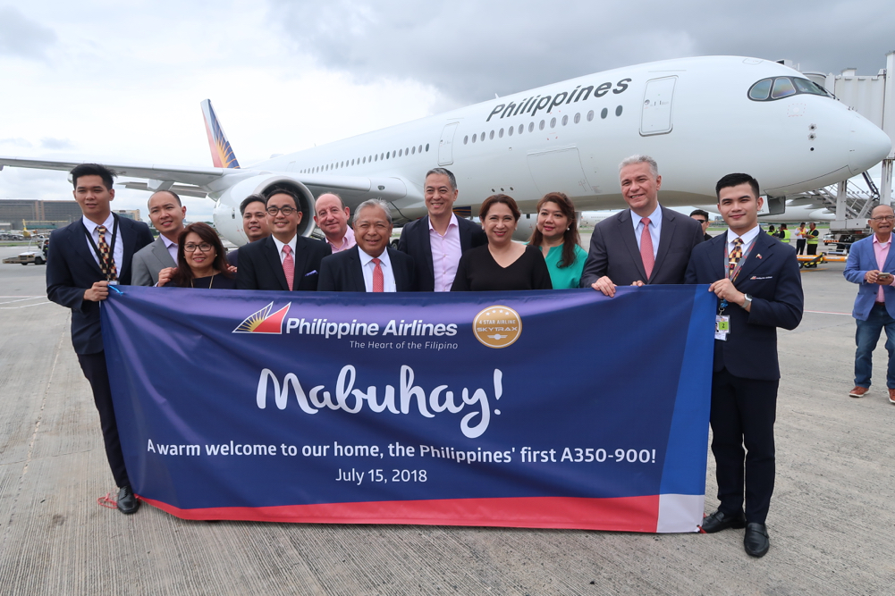 a group of people posing for a photo with a banner in front of an airplane